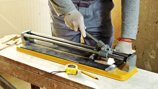 Person using a yellow manual tile cutter on workbench