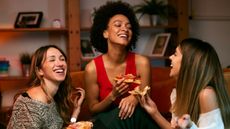 Three young women laugh as they eat pizza.