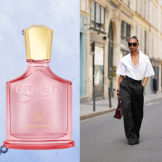 A woman wearing a white top and black pants next to a bottle of perfume. 