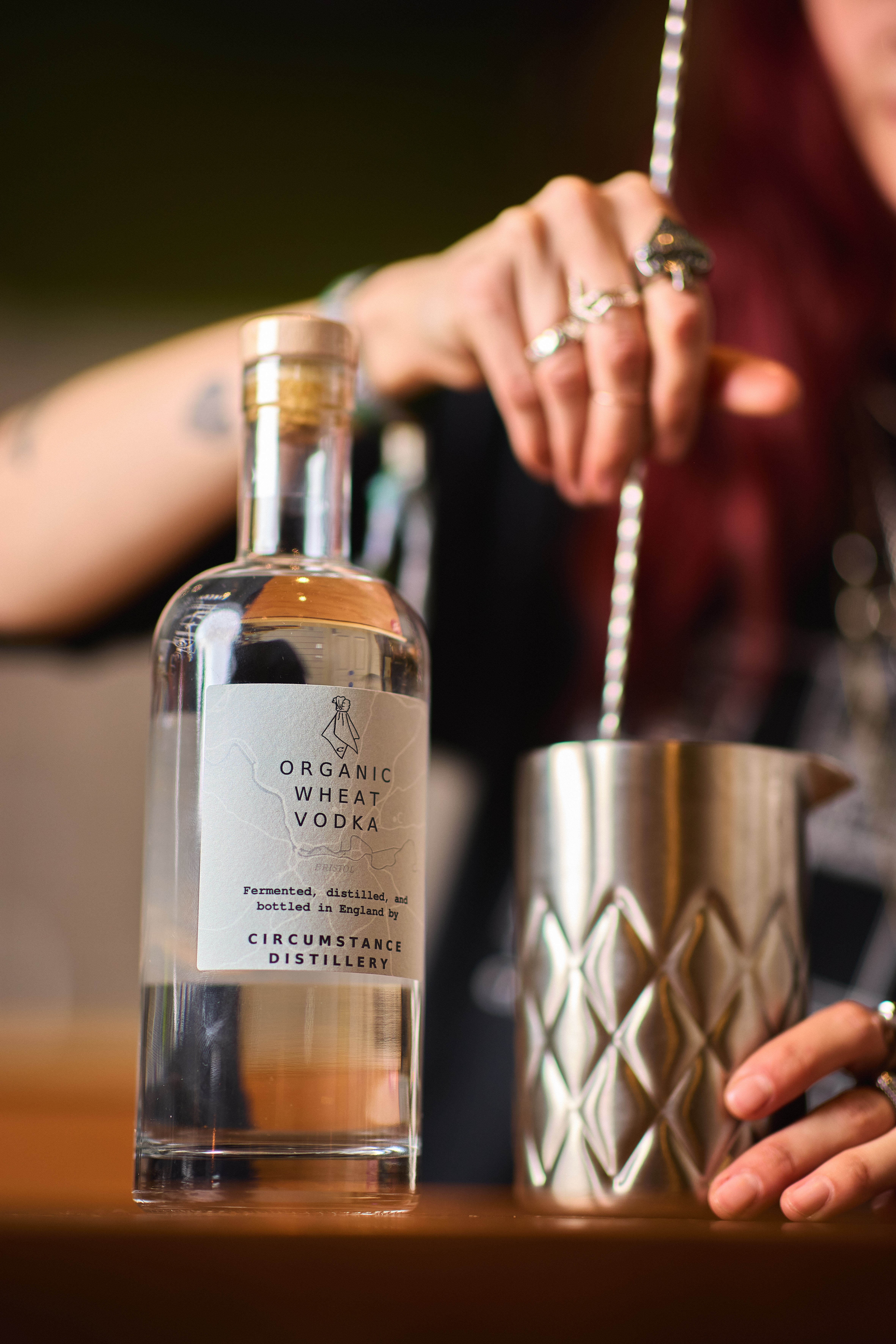 A bottle of vodka in the foreground and a close-up of a woman stirring a cocktail in the background