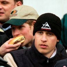 Princes Harry eats a burger while Prince William watches on during the IRB Rugby Aid Match between The Northern Hemisphere and The Southern Hemisphere at Twickenham Stadium on March 5, 2005 in Twickenham, England