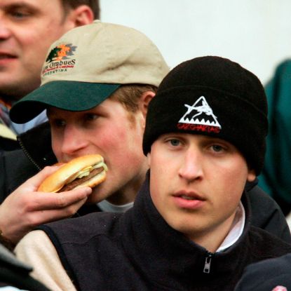 Princes Harry eats a burger while Prince William watches on during the IRB Rugby Aid Match between The Northern Hemisphere and The Southern Hemisphere at Twickenham Stadium on March 5, 2005 in Twickenham, England