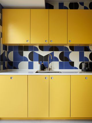 yellow kitchen cabinets with blue and white geometric print backsplash tiles