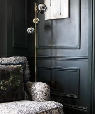 A black-painted living room with a floral-print armchair and a chrome floor lamp