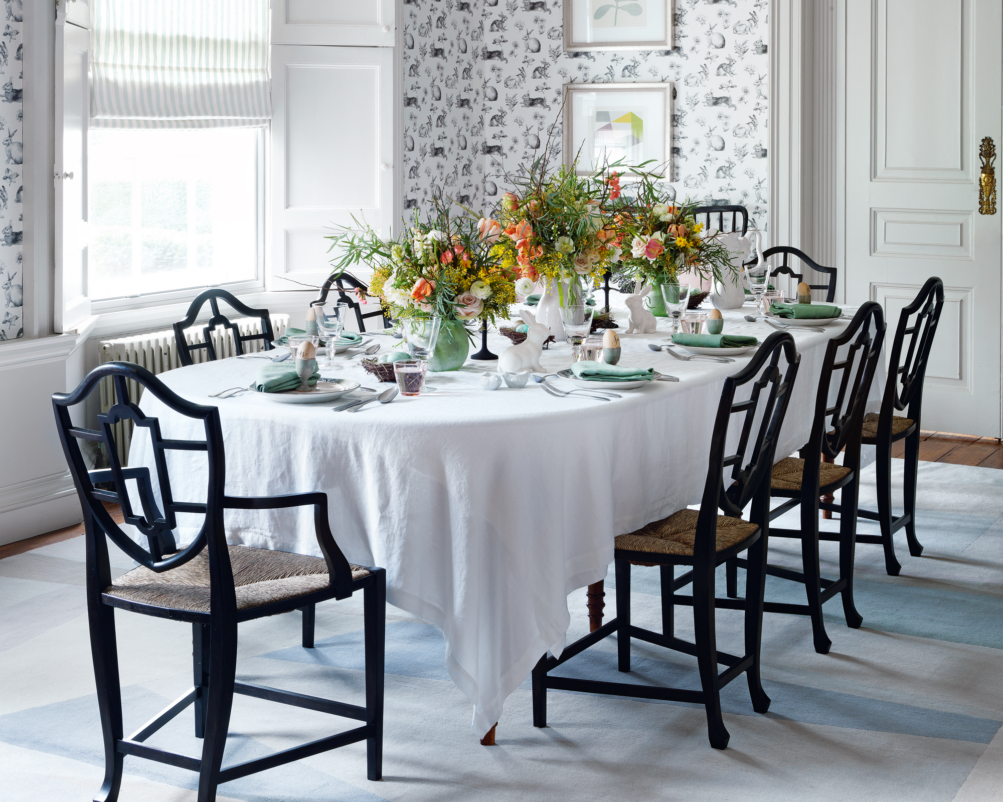 A dining table decor idea with an Easter theme and three bunches of orange and yellow flowers running down the table