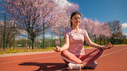 Women sits on an athletic track in a meditative pose