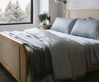 Blue bamboo bed sheets on a wood bed frame against a white wall.