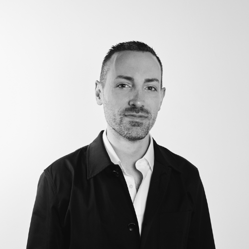 Black and white image of a man in a white button down shirt and black jacket.