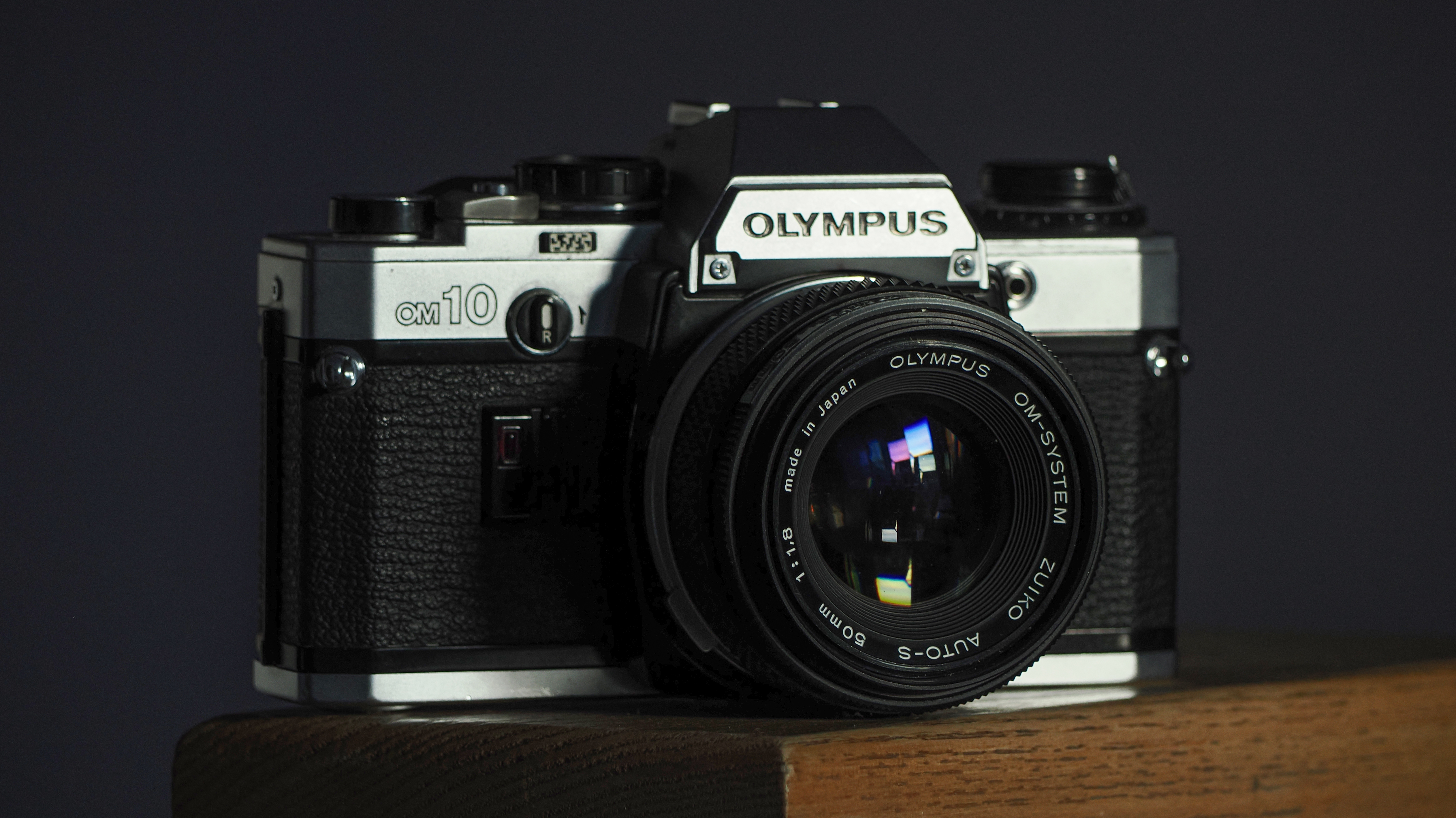 Olympus OM-10 with an Olympus Zuiko 50mm f/1.8 on a wooden surface in front of a dark background