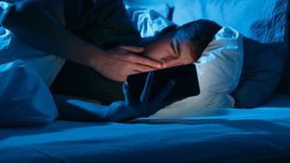 A man looks at his phone, which is giving off blue light, whilst in bed