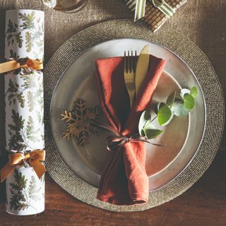 A dining table set for a Christmas dinner with an orange napkin placed on top of the plates and tied around the cutlery