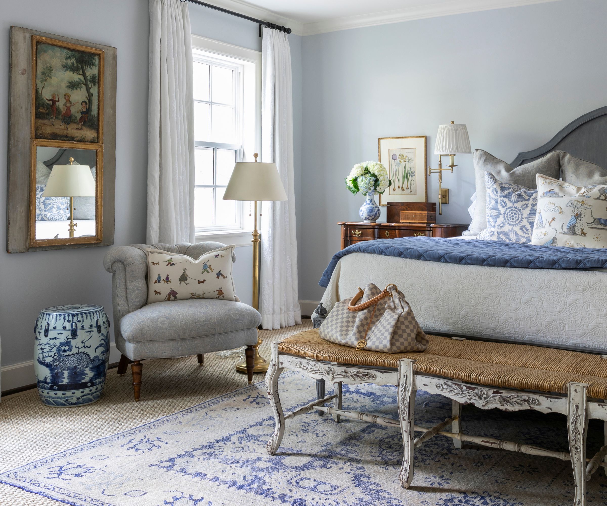 preppy blue and white bedroom with a whitewashed rustic bed, blue and white rug, a chinoiserie stool, antique chest nightstand styled with hydrangeas