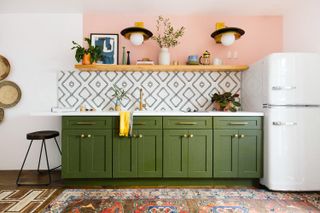 green kitchen cabinets with black and white tiled backsplash and peach wall