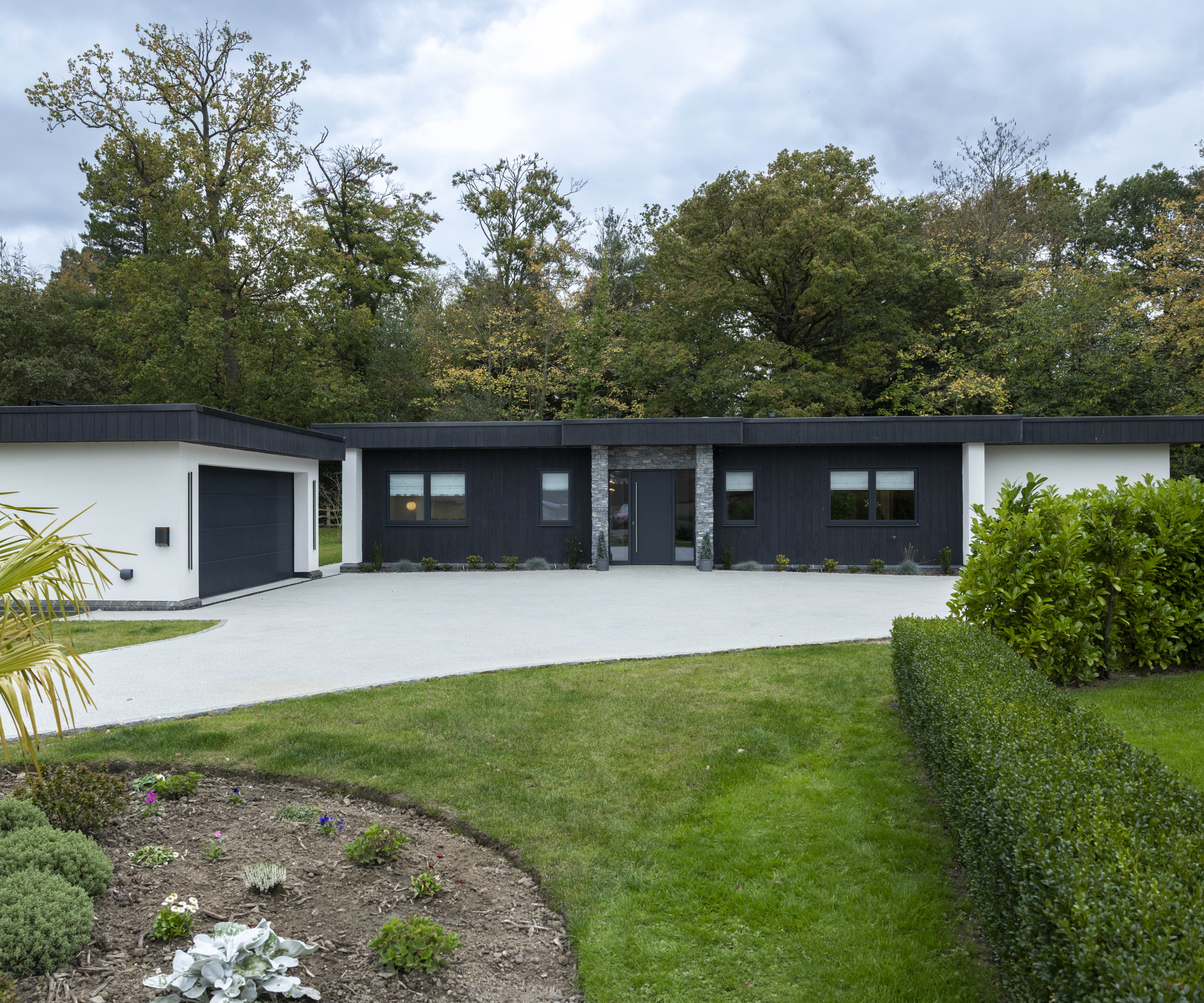 modern single storey home with black roof and cladding, white render and large modern driveway and garden