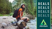 Woman with trekking poles sitting beside stream