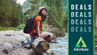 Woman with trekking poles sitting beside stream