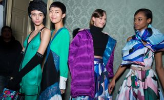 Models wear turquoise dresses, whilst another wears a bright purple puffer coat