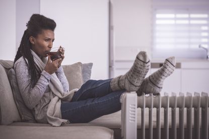 Woman drinking hot tea, heating feet at home
