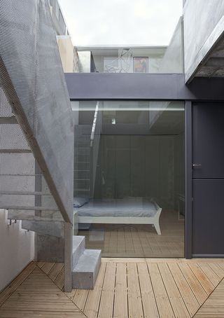 Wooden flooring with steel staircases. A closed black door leading to a bedroom with a view of the double bed with white bed frames, grey sheets and pillow case