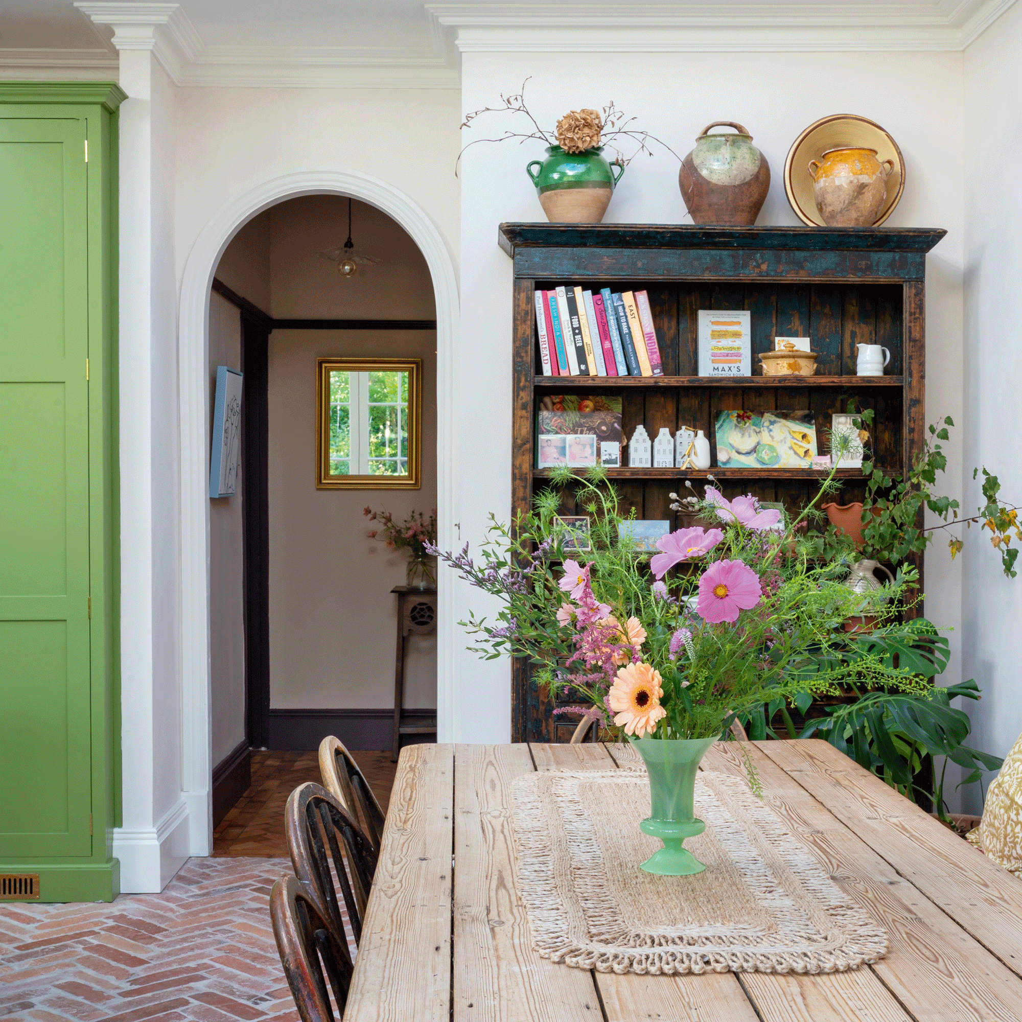 a green kitchen with a rustic dining table and bookshelf