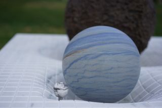 A pale blue sphere with blue striations sits within an indented piece of marble.
