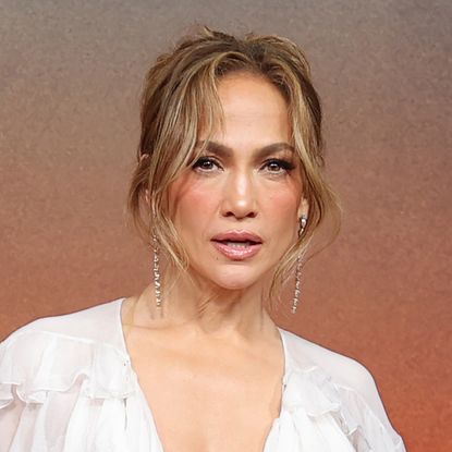 Jennifer Lopez wears a white tassled dress and stands in front of a sunset
