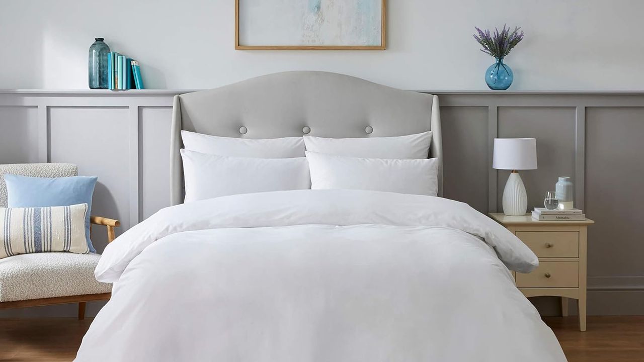 A bedroom with a bed covered in white bedlinen and a wooden armchair to one side