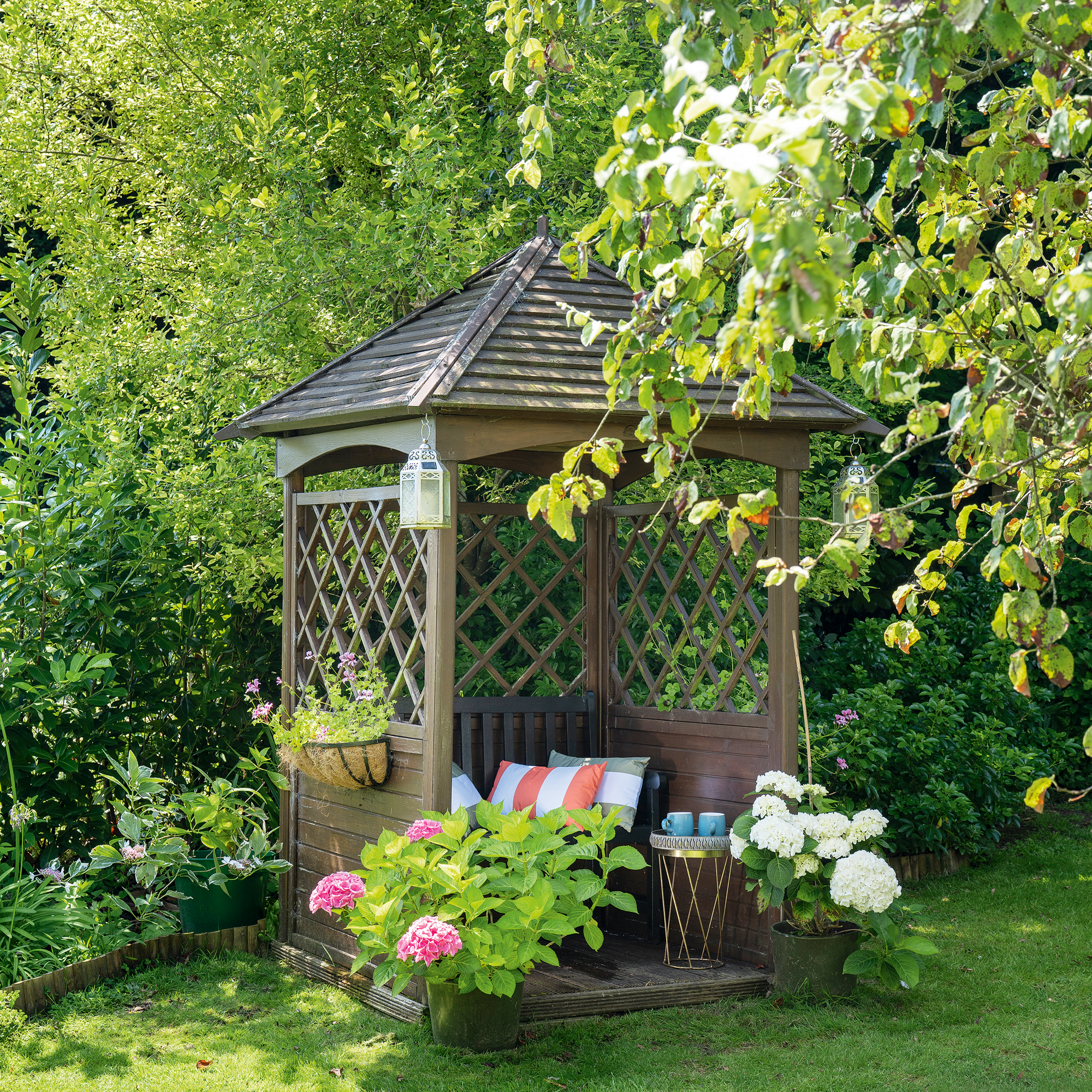 a garden with a bower with cushions and potted hydrangeas