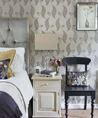 bedroom with grey designed wallpaper white drawer and chair with cushion