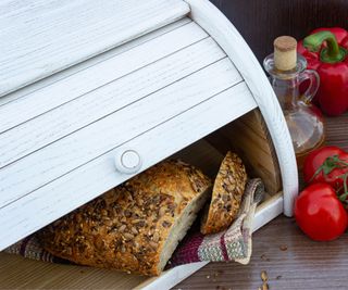 A wooden bread box with bread inside and tomatoes on the outside