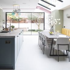 A modern kitchen diner in Victorian Terrace house with olive green kitchen cabinetry, blue kitchen island, light grey dining set and yellow banquette seating
