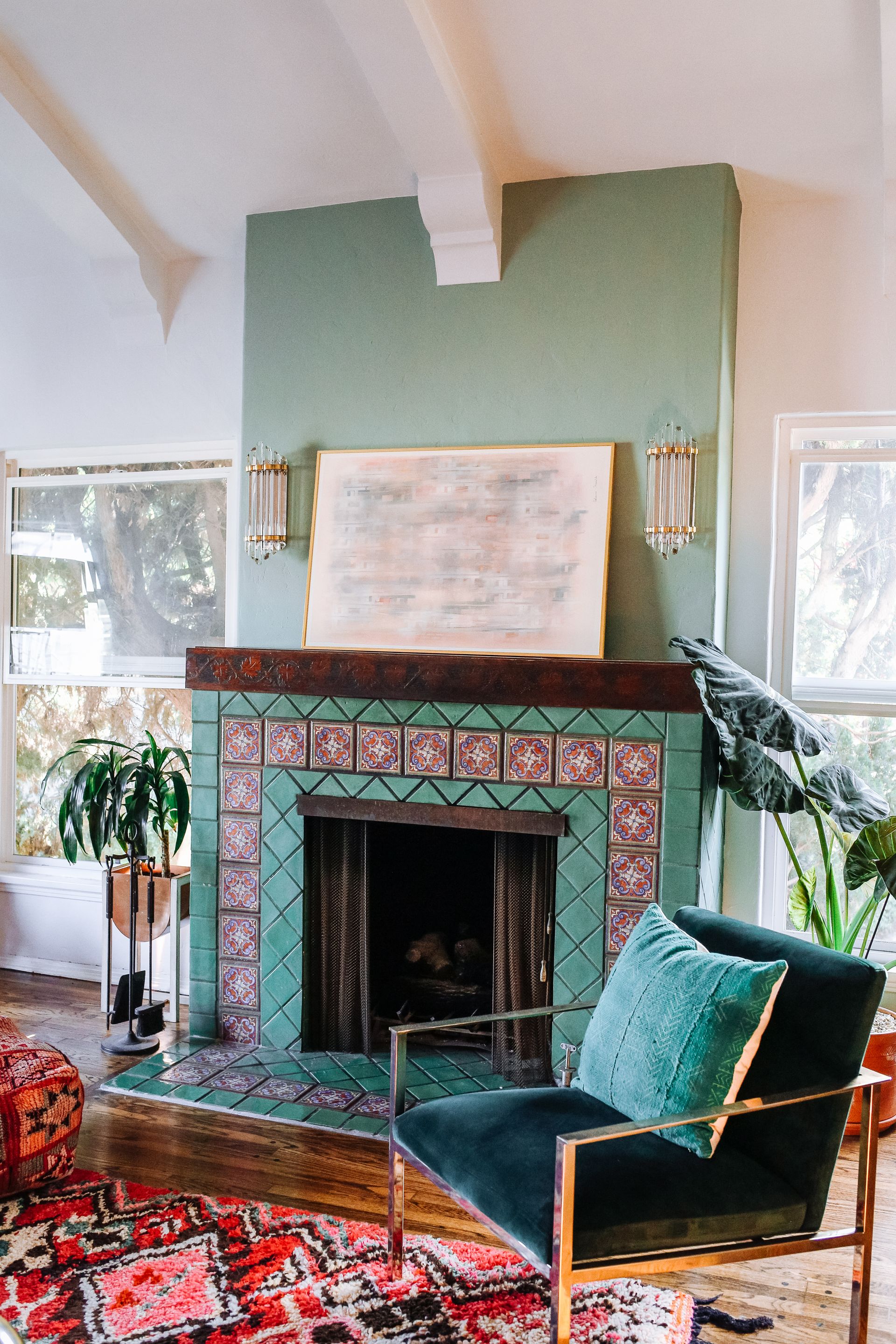 Living room with sconces above mantel on green chimney, armchair, rug and wood floor