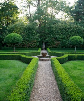 parterre of box hedging with gravel paths around a fountain and statue at far end