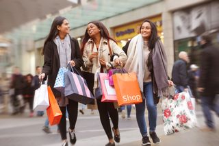 three women walking down a high street laughing and carrying shopping bags