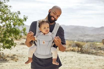 A smiling man outdoors carrying a baby in the Ergobaby Omni Dream Baby Carrier