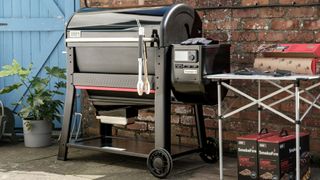 The Weber Searwood XL 600 against a brick wall with a blue gate in the background.