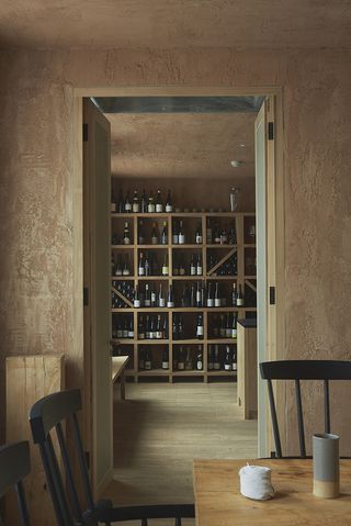 Wooden doorway in a bare plaster wall looking into a wooden wall display of wine bottles and glasses