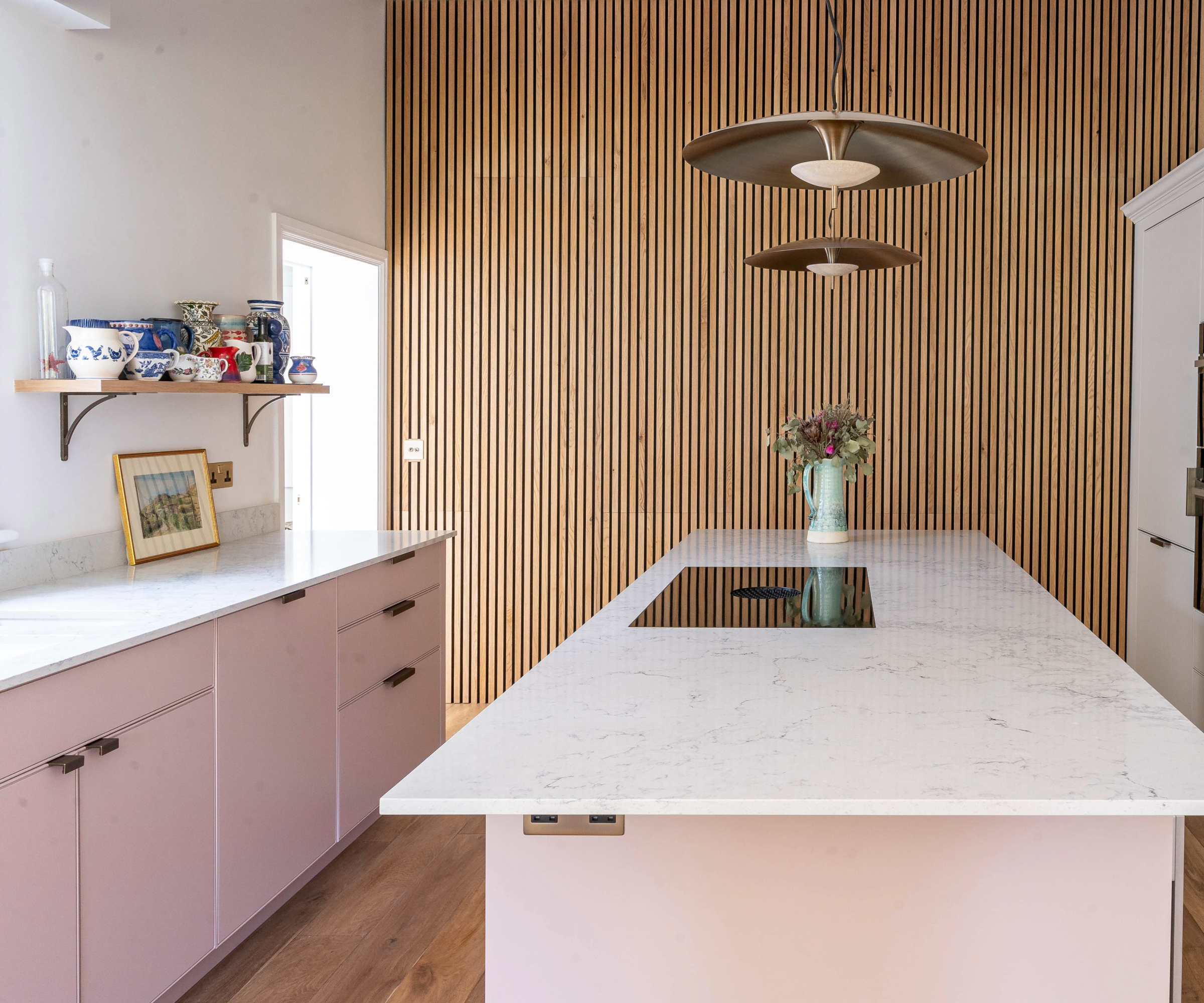 Pink kitchen with white marble work top and wooden panel feature wall