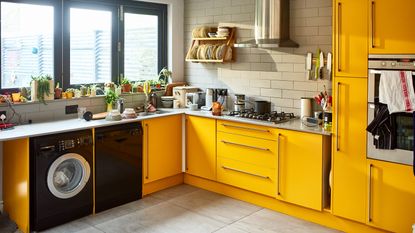 A retro domestic kitchen with yellow kitchen cabinetry and doors and black washing machine appliance