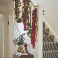 A white hallway staircase with a striped runner and decorated for Christmas with a pre-lit garland and red bows