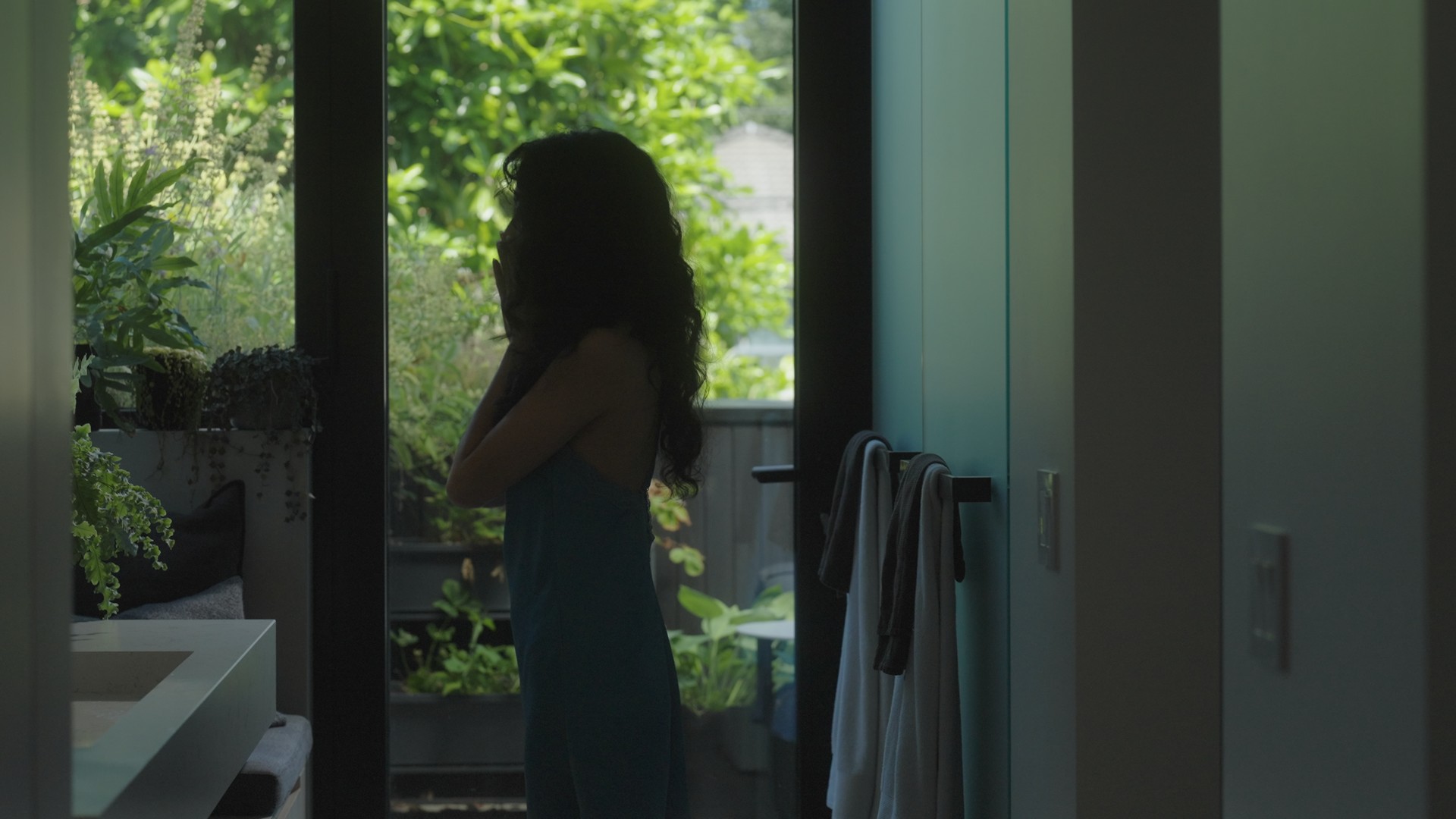 A woman stands in front of a green garden at a backdoor in Prove You're Human