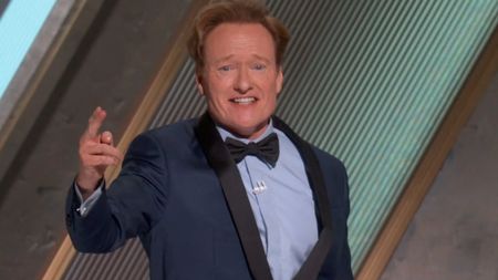 Conan O'Brien smiles in mid salute while wearing a blue tux at the 97th Academy Awards.