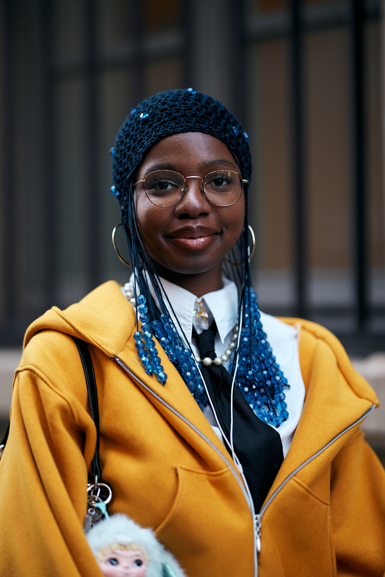 a woman wearing a yellow jacket, white shirt and black tie with glasses and blue beads in her braids