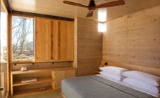Bedroom with wooden walls, double bed and window with view of desert 