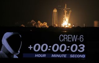 a rocket lifts off behind the famous countdown clock at Kennedy Space Center