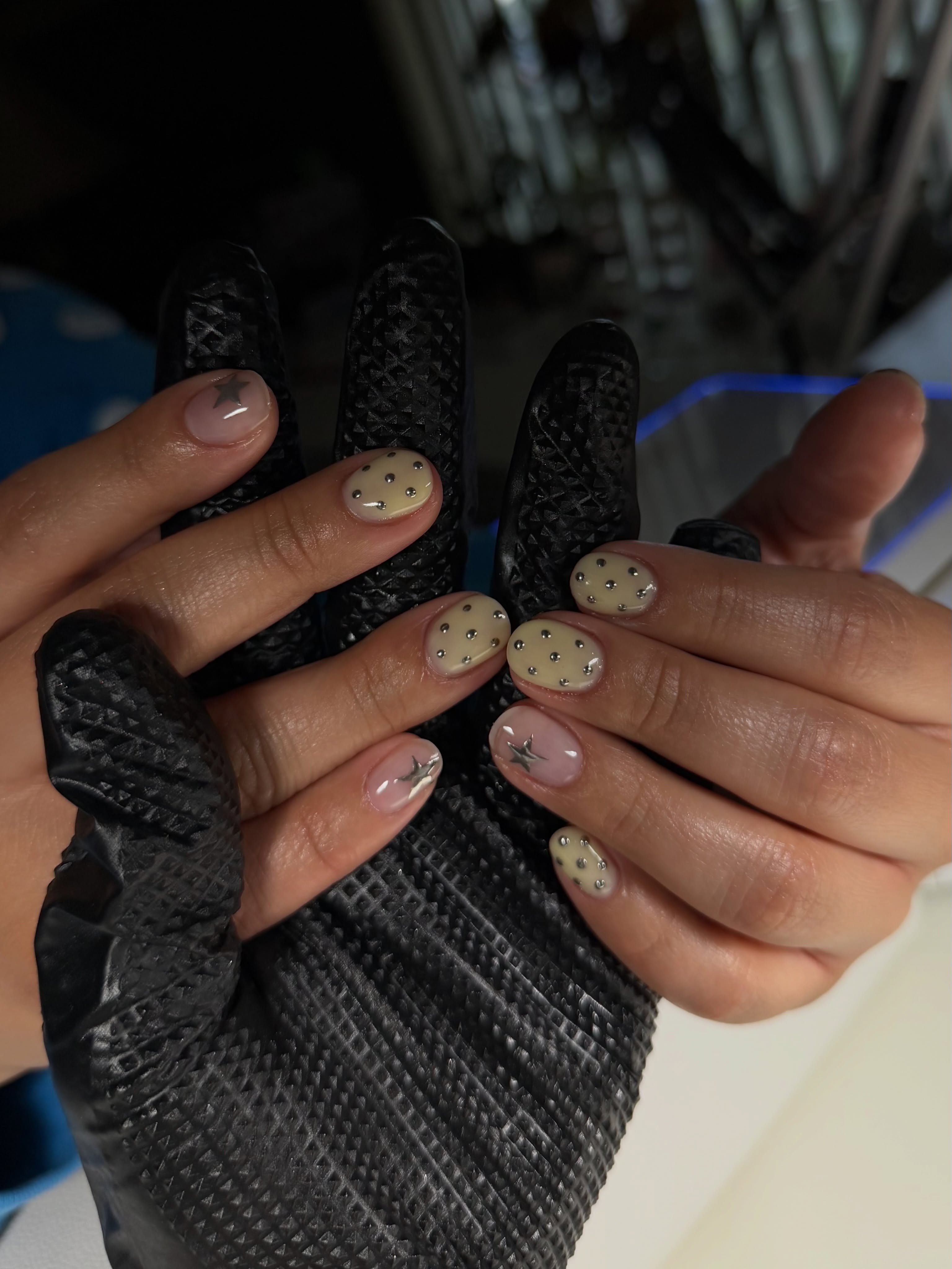 Short nails in sheer pink and pale butter yellow with tiny silver studs and metallic star details