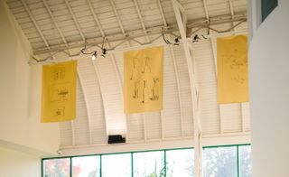 Sketches on three sheets of yellow paper hang from the roof