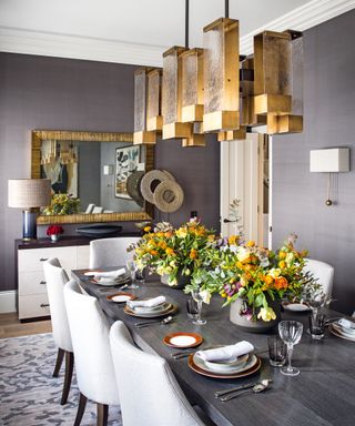 A dining table decor idea with modern brass chandelier, dark grey walls and yellow and orange floral arrangements