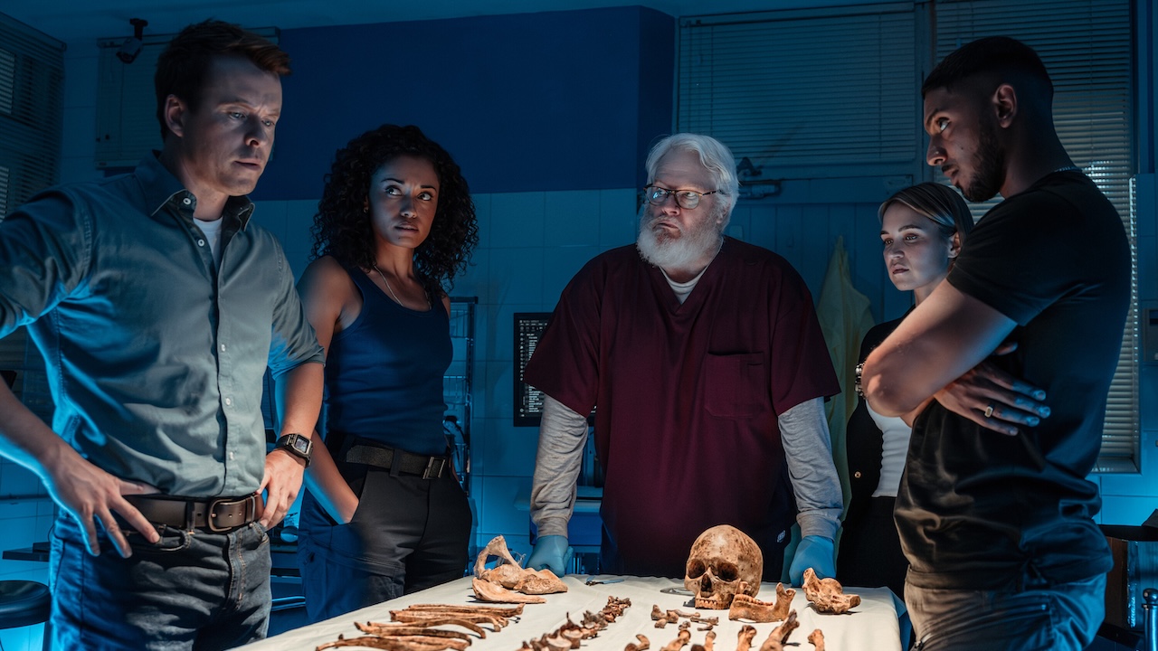 JD, Mackey, Rosie, Evie and DeShawn standing around a table with a skull and various bones on it in NCIS: Sydney