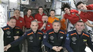 11 astronauts in blue and red flight suits hold a welcome ceremony on the international space station